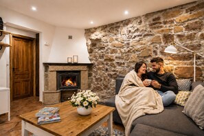 Un salon chaleureux avec un mur en pierre, une cheminée, un canapé, une table basse et un couple assis ensemble.