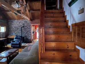 A wooden staircase leading to a loft area with a stone wall and a sofa.