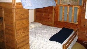 Une chambre dans un chalet en bois, avec un lit superposé, une fenêtre avec des stores et un luminaire suspendu.