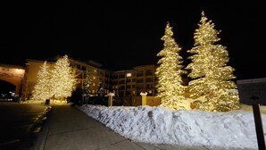 Entrada de hotel con árboles de Navidad iluminados y un sendero cubierto de nieve.