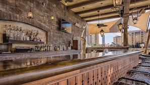 A bar with a wooden counter and stools, a brick wall, and hanging lights.