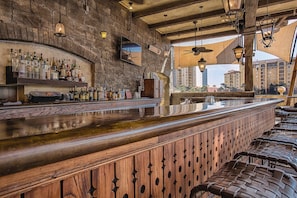 Relax in a warm and inviting space with a wooden bar counter and seating area, offering a selection of drinks and a view of the surrounding buildings.