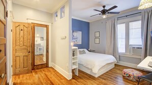 Une chambre à coucher avec un lit, un ventilateur de plafond, une fenêtre avec des rideaux et un plancher en bois.