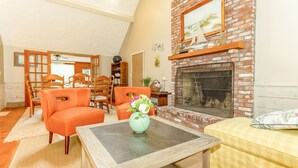 Una sala de estar con chimenea, sillones naranjas, una mesa con un florero y un sofá amarillo.