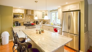 Una cocina moderna con una isla grande, electrodomésticos de acero inoxidable e iluminación colgante.