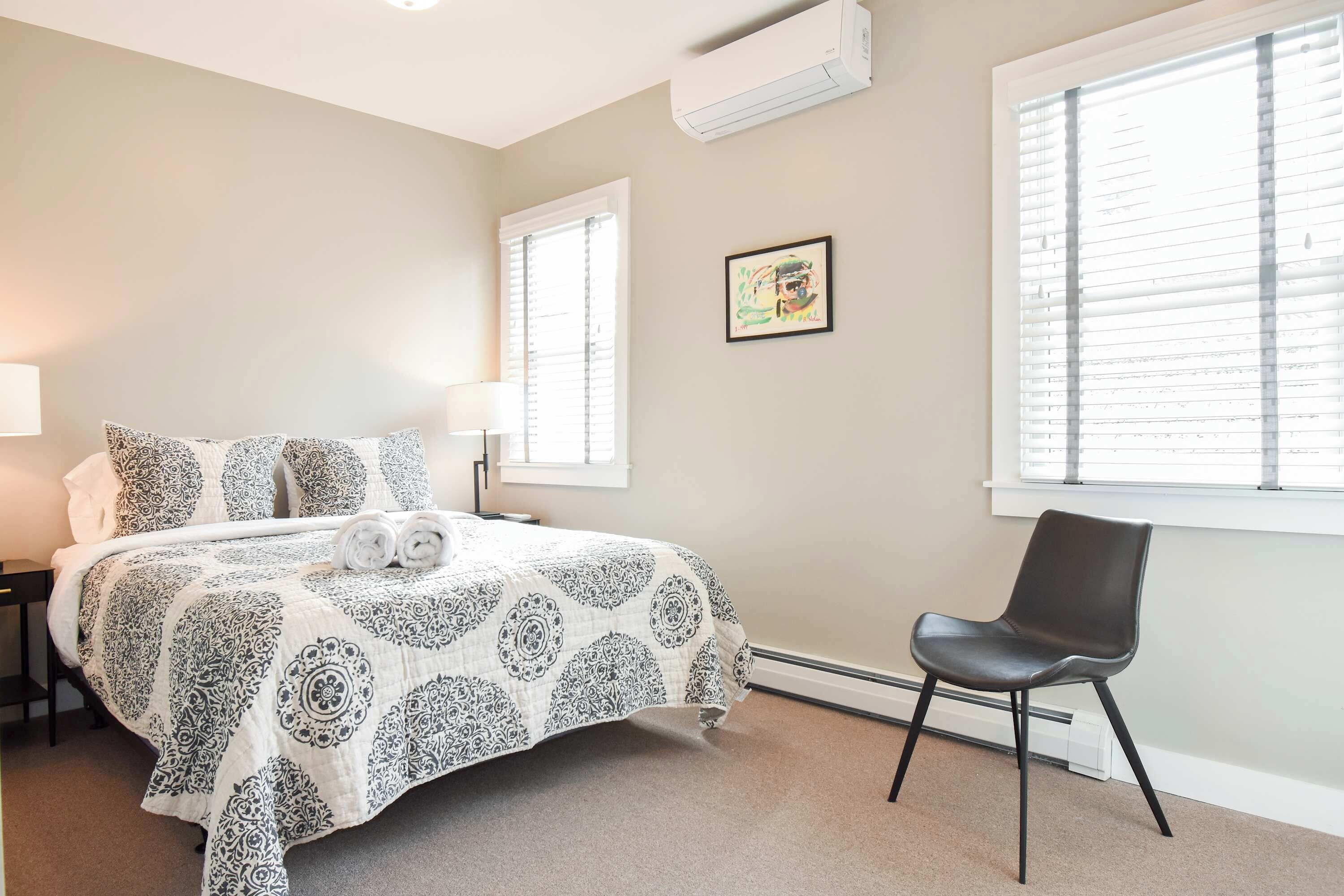 A bedroom with a bed, a chair, and a window with blinds.