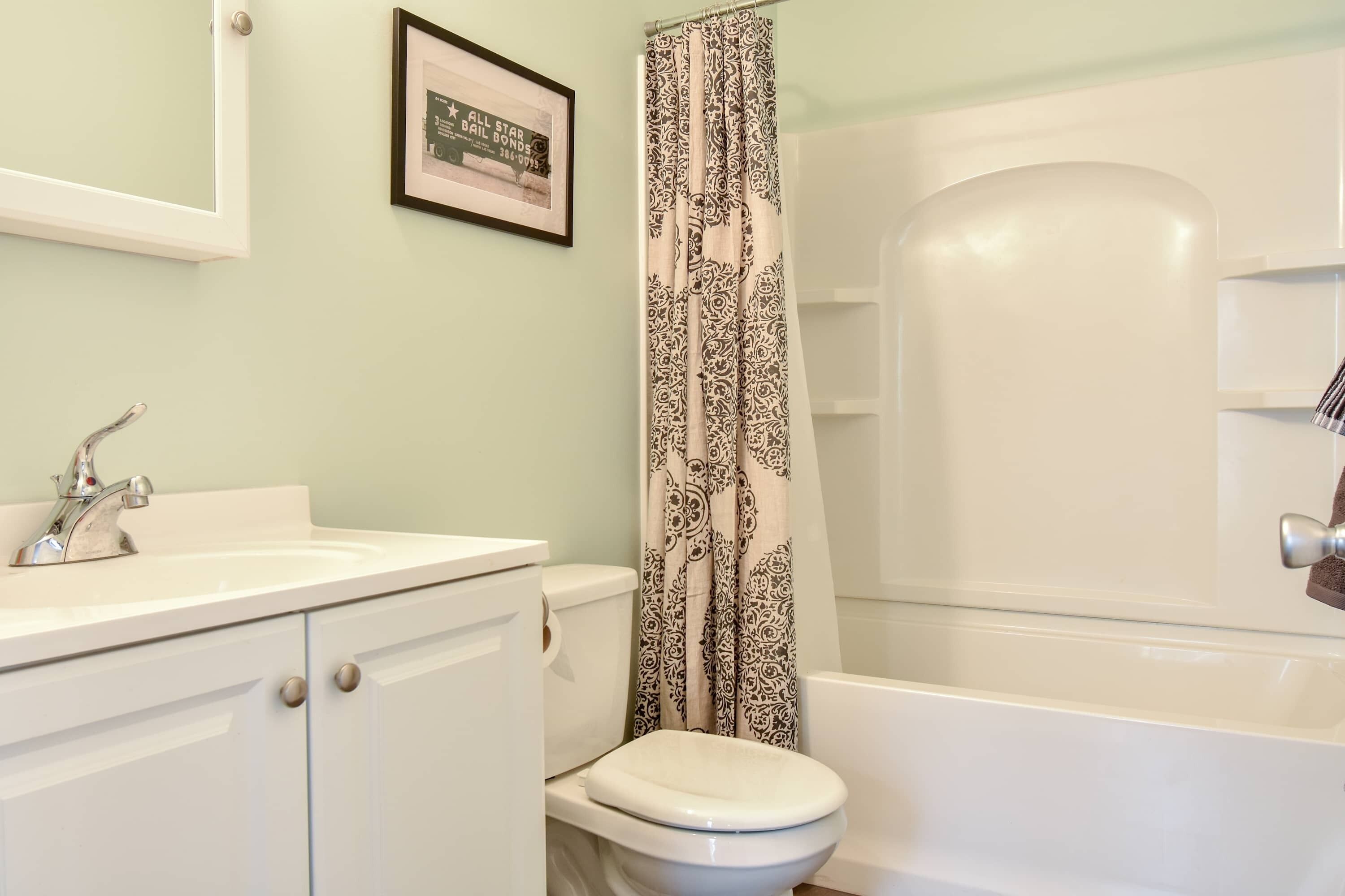 Ein Badezimmer mit einem weißen Waschbecken, einer Toilette und einer Badewanne. An der Wand hängt ein gerahmtes Bild.