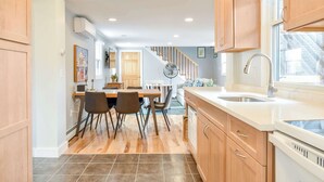 A modern kitchen with wooden cabinets, a dining area with chairs, a staircase, and a large window.