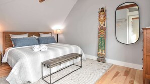 A bedroom with a bed, bench, wall-mounted mirror, and a decorative item.
