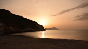 Une plage au coucher du soleil, avec une eau calme et une falaise rocheuse.