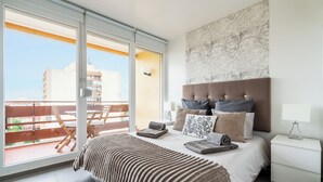 Un dormitorio con un ventanal grande, una cama con ropa de cama a rayas, un cabecero y una mesita de noche.