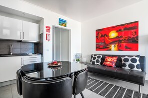 Une cuisine moderne avec des meubles blancs, une table à manger noire et un canapé noir agrémenté de coussins à motifs.