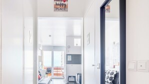 Un pasillo moderno con una puerta de marco negro, un letrero que dice 'THIS IS OUR HAPPY PLACE', y vistas a una sala de estar con un sofá y una mesa de comedor.