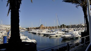 Un puerto deportivo con numerosas embarcaciones amarradas, un cielo azul despejado y un edificio con un techo característico al fondo.