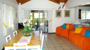 A dining area with a wooden table, chairs, and a potted plant. There is a bright orange couch with blue pillows.