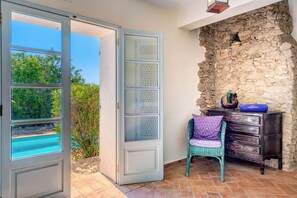 An open door leading to a pool, a stone wall, a wicker chair, and a wooden dresser with a blue bowl on top. - Private villa with private garden, pool and sea view (Olhao,)