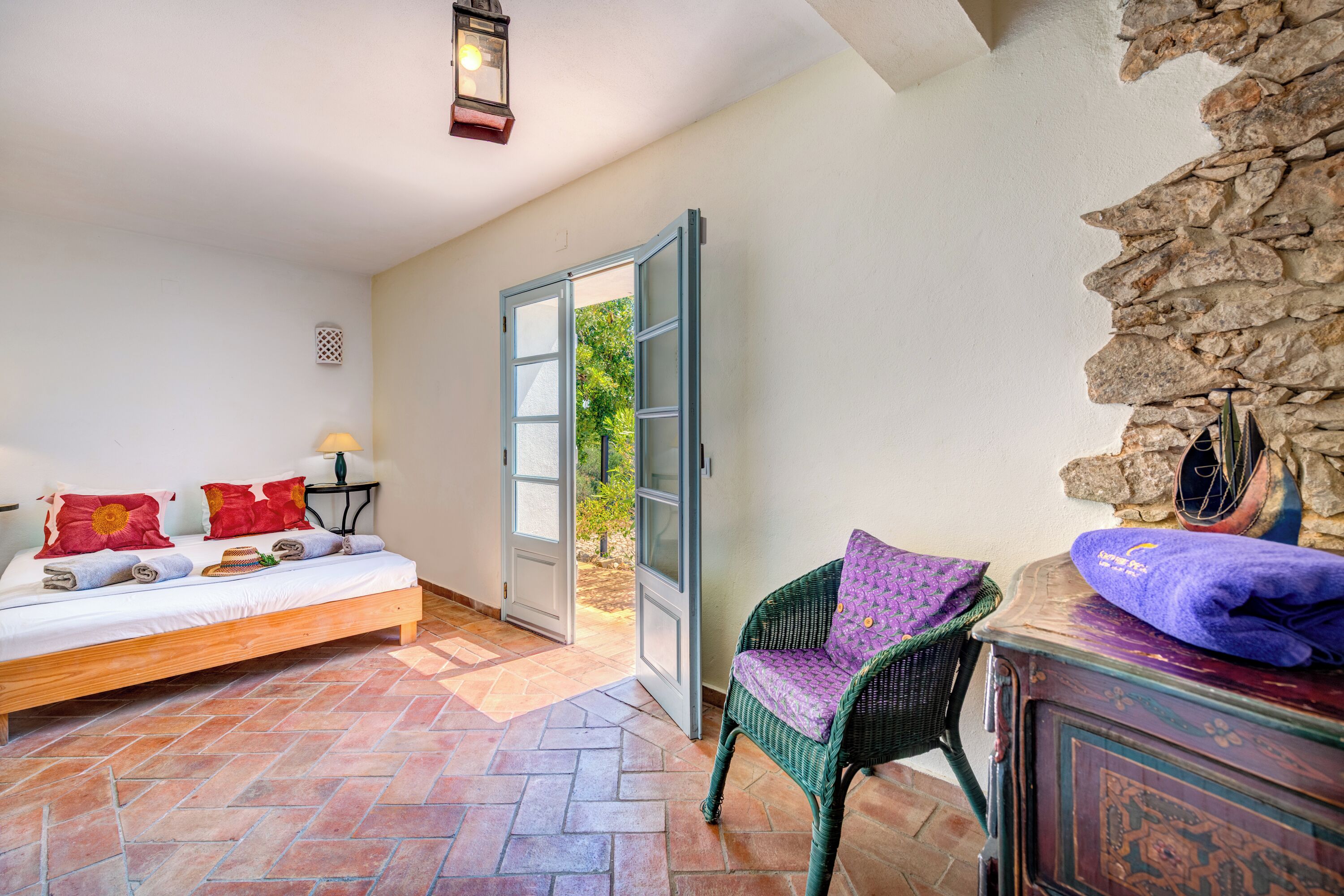 Une pièce avec un lit, une chaise, une lampe et un mur en pierre.