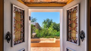 Puerta abierta que da a un balcón con vistas a vegetación y un muro de piedra.