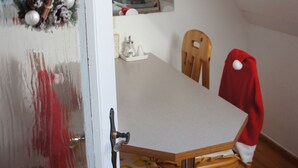 A dining area with a wooden table and chairs, a red jacket hanging on one chair, and a Christmas wreath on the door.