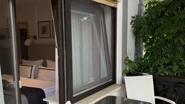 A balcony with a table and two chairs, a bed with a headboard, and a door leading to a room.