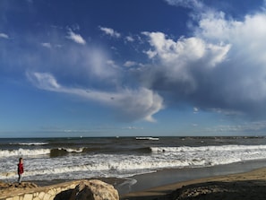 Une plage avec des vagues, une personne portant une veste rouge et un mur de pierres.