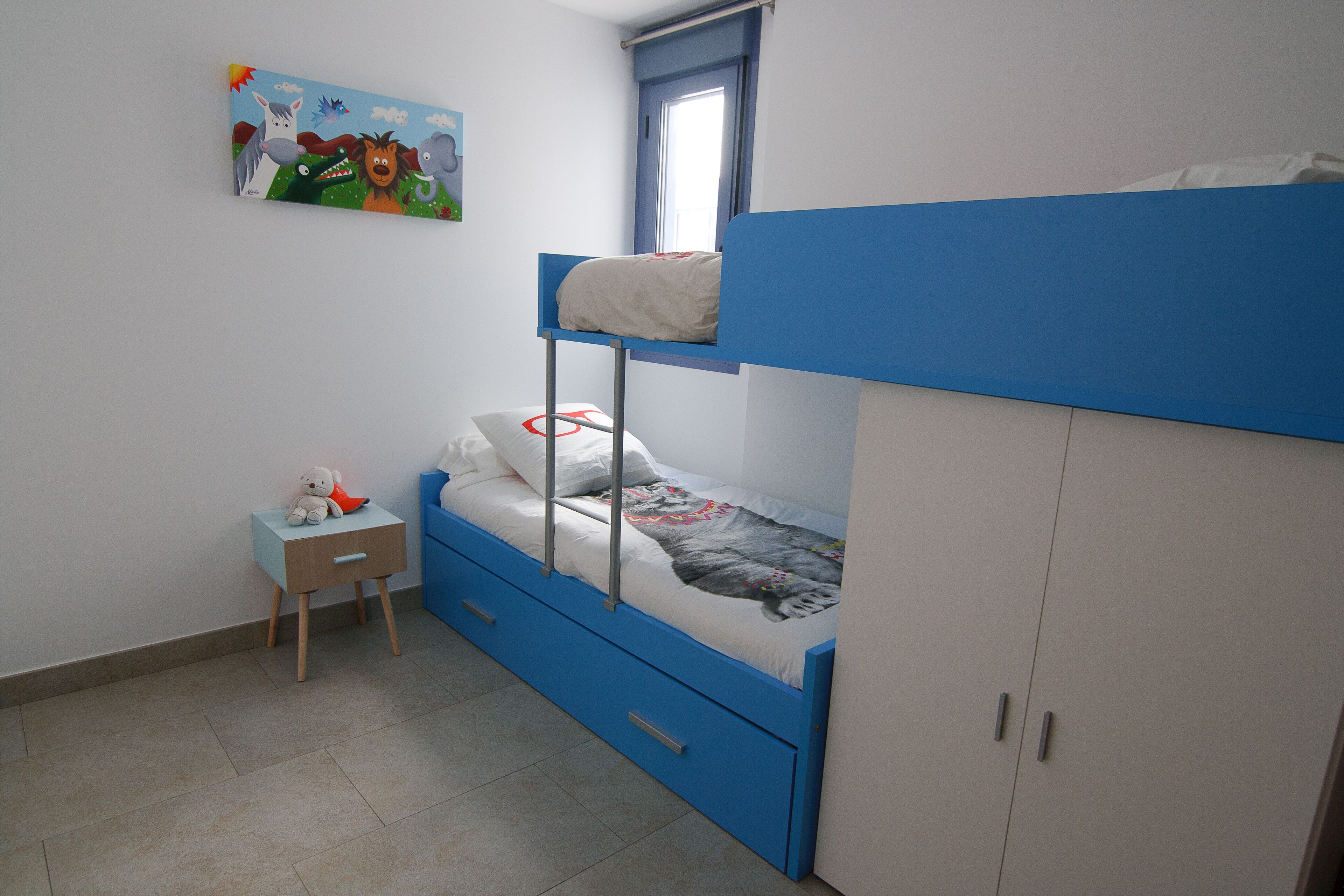 A bunk bed room with a small bedside table, a chair, and a painting on the wall.