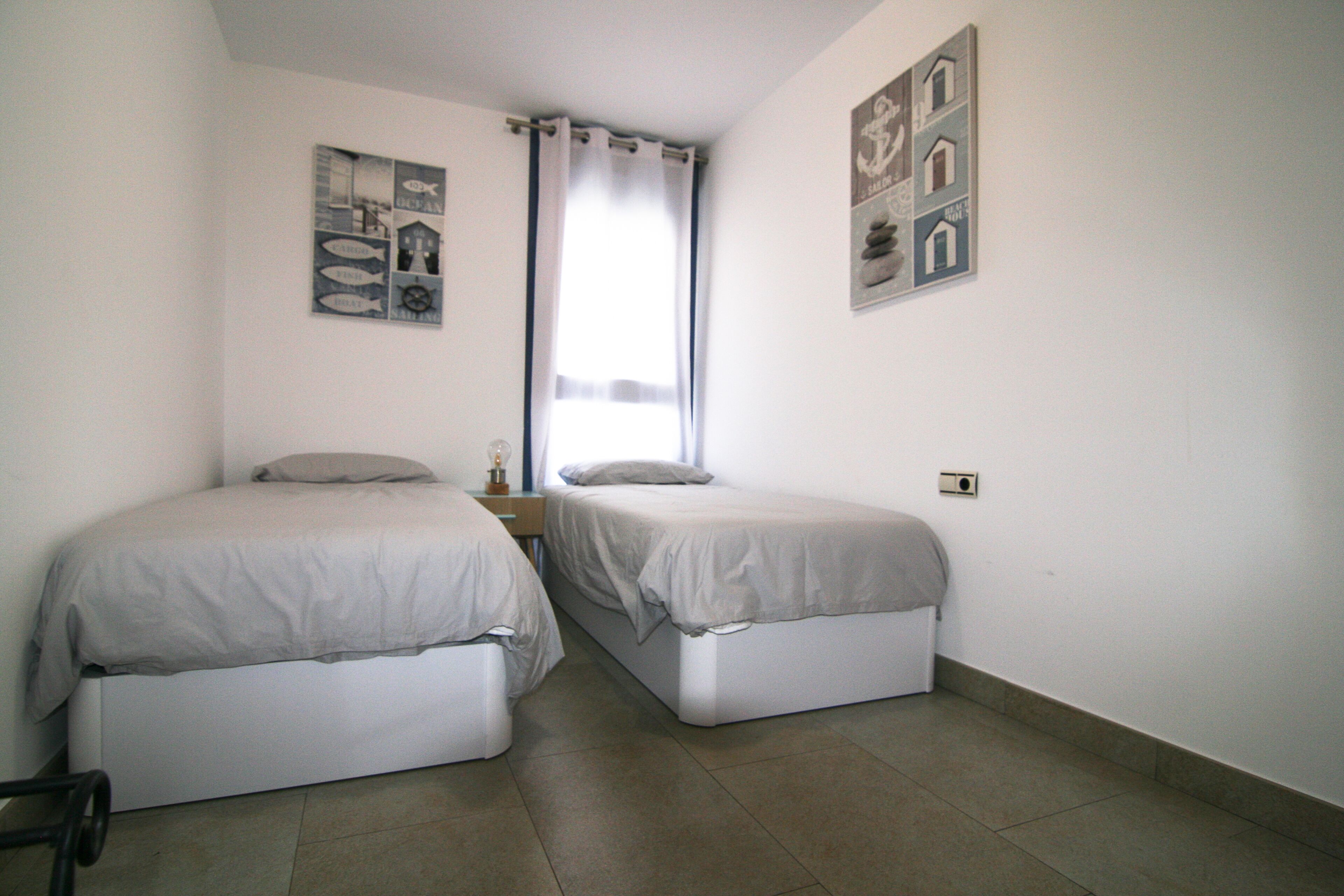 Una habitación pequeña y limpia con dos camas individuales, una ventana con cortinas y decoración de temática náutica.