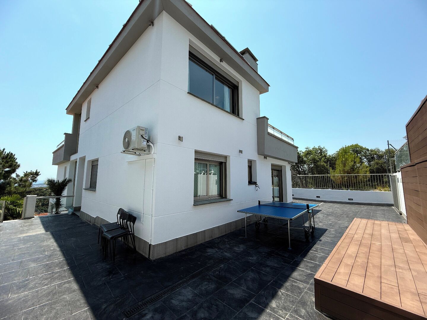 A modern two-story house with a flat roof, a large window, and a small balcony.
