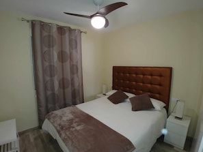 Ein Schlafzimmer mit einer gepolsterten Kopfteile, einem Bett mit weißer und brauner Bettwäsche, einem Nachttisch mit Lampe und einem Deckenventilator.