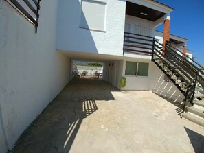 Ein Gebäude mit überdachter Terrasse, einer Treppe und einem sichtbaren Gartenschlauch.
