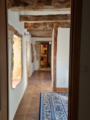 A hallway with exposed wooden beams, a patterned rug, and a view into a room with a bed and a nightstand. - Period Farmhouse, sleeps 12, large 12m x 6m pool, barn, big garden, courtyard (Verfeil)