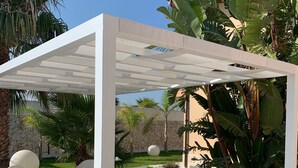 A covered outdoor seating area with a table and chairs, surrounded by lush greenery and palm trees. - Holiday home with garden near Balestrate Beach (balestrate)