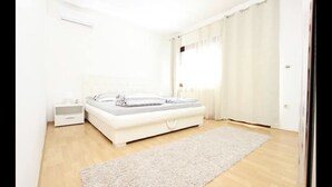 A bedroom with a bed, bedside tables, a nightstand, a window with curtains, and a wooden floor. - Apartment Ria, Apartments Pejton Ilidža Sarajevo (Sarajevo)