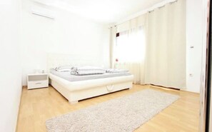 Un dormitorio con cama, mesitas de noche, una ventana con cortinas y suelo de madera.