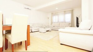 A modern living room with a white sofa, a glass coffee table, and a dining area with a white table and chairs. - Apartment Ria, Apartments Pejton Ilidža Sarajevo (Sarajevo)