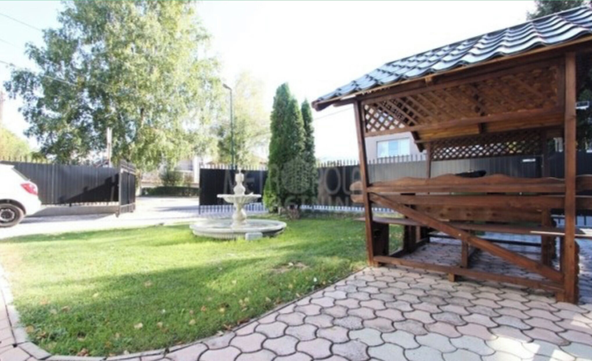 En uteplats med ett klinkergolv, en träpergola och en fontän.