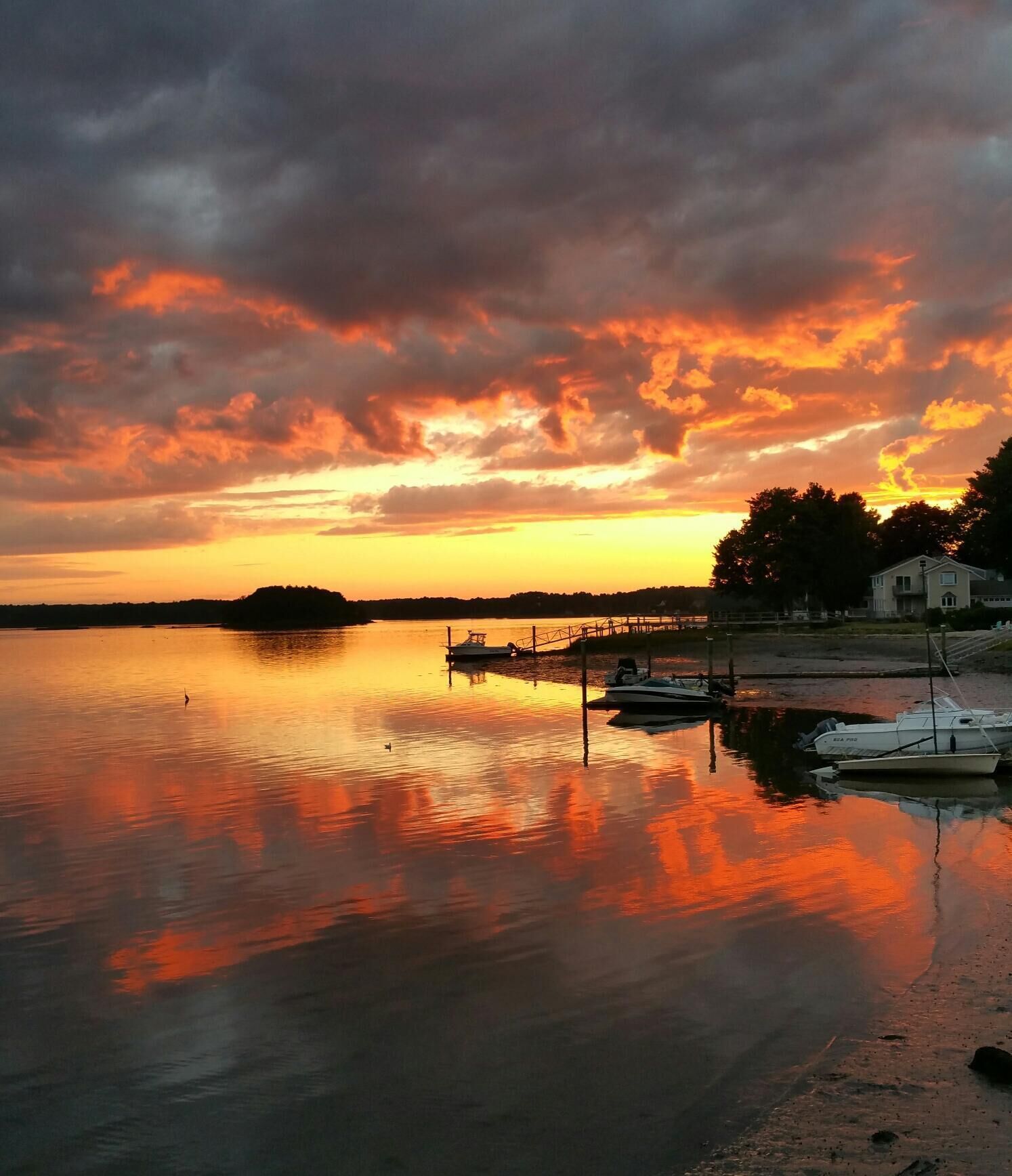 Um lago calmo ao pôr do sol, com barcos atracados na margem e uma casa ao fundo.