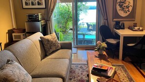 A cozy living room with a sofa, a coffee table with books, a dining area with chairs, and a view of a garden through a sliding door. - Lovely Waterfront Suite near Portsmouth (Dover)