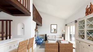 A spacious living room with a high ceiling, a staircase, wicker furniture, a white sofa, and a glass cabinet. - Provençal 10 people villa with heated pool and panoramic sea view (Mandelieu-la-Napoule)
