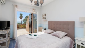 A bedroom with a large bed, a TV, a chandelier, and a sliding glass door leading to a balcony. - Provençal 10 people villa with heated pool and panoramic sea view (Mandelieu-la-Napoule)