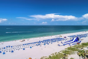 A beach with a water slide and numerous blue lounge chairs. - Walk to Beach | Parking Space Provided (St. Pete Beach)