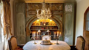 Un coin repas avec une table en marbre, des chaises décorées, un lustre et une bibliothèque remplie de livres et de bougies.