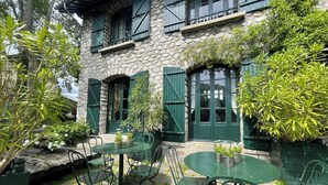 Un bâtiment en pierre avec des volets verts et une terrasse dotée de mobilier en métal vert.