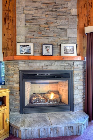A stone fireplace with a fire, framed pictures above it, and a wooden shelf.