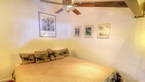Ein Schlafzimmer mit einem Bett, einem Deckenventilator und gerahmten Bildern an der Wand.