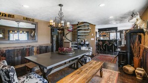 Een rustiek interieur met een houten bar, een kroonluchter, een wenteltrap en een eetgedeelte met een houten bank en een kamerbreed tapijt.