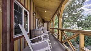 Een overdekte veranda met houten leuningen, witte schommelstoelen en houten vaten.