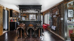 Een rustieke bar met houten barstoelen, een zwarte toog en een plafond in vintage-stijl.