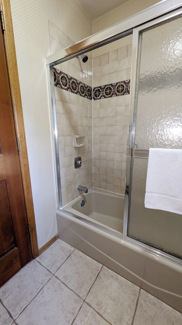 A walk-in shower with a glass door, tiled walls, and a white towel hanging on the door.