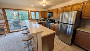 A kitchen with wooden cabinets, a stainless steel refrigerator, a microwave, and a large island with stools.
